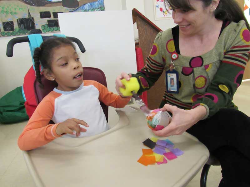 With the assistance of Art Teacher Amanda Wakely, Washington Center student Prasia Taylor decoupages with tissue paper to make an ornament for the holidays.